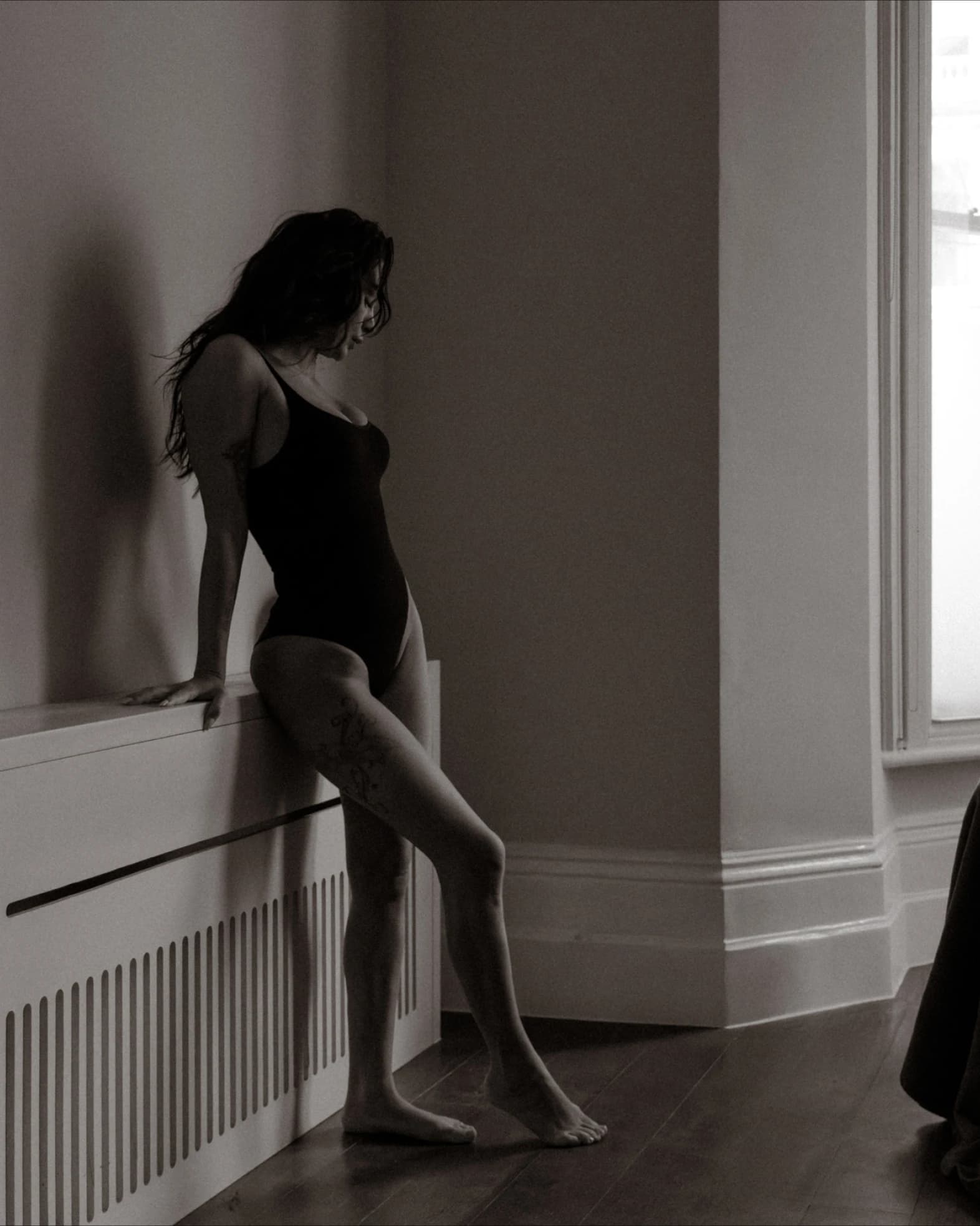 Moody boudoir photo of a woman in a bodysuit leaning against a wall